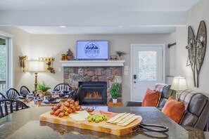 A kitchen with a stone fireplace, a dining area with chairs, and a TV displaying 'BOULDER ROCKS'.