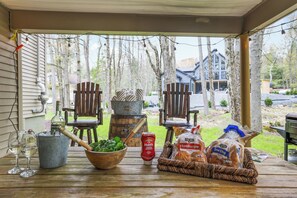 A wooden table with a bowl of greens, a bottle of ketchup, wine glasses, and packaged food items.