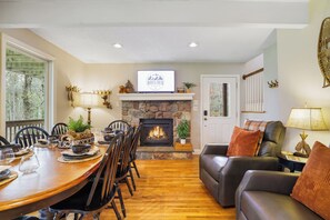 A dining area with a fireplace, a living room with a sofa, and a television mounted above the fireplace. - Sleeps 14! Wooded Retreat, Prime Location, Lake Access With Hot Tub (Lake Harmony)