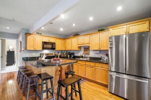 A kitchen with wooden cabinets, a stainless steel refrigerator, and a bar area with stools.
