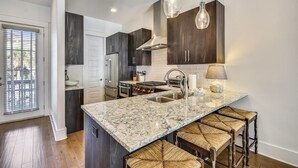 A modern kitchen with dark wood cabinets, a granite countertop, and a built-in stove. There are three hanging pendant lights and a window with blinds. - Amazing pet-friendly family getaway w/elevator, game room, 7 bikes, & EV charger (Seacrest Beach)