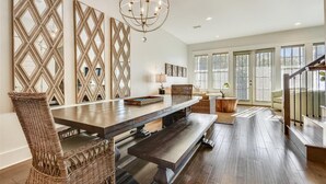 A spacious dining area with a long wooden table, wicker chairs, and a chandelier. - Amazing pet-friendly family getaway w/elevator, game room, 7 bikes, & EV charger (Seacrest Beach)