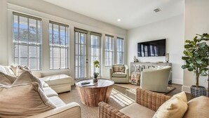 A spacious living room with a large TV, comfortable seating, and a view through large windows. - Amazing pet-friendly family getaway w/elevator, game room, 7 bikes, & EV charger (Seacrest Beach)