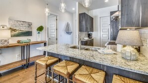 A modern kitchen with a marble island, bar stools, pendant lighting, and a view of the dining area. - Amazing pet-friendly family getaway w/elevator, game room, 7 bikes, & EV charger (Seacrest Beach)