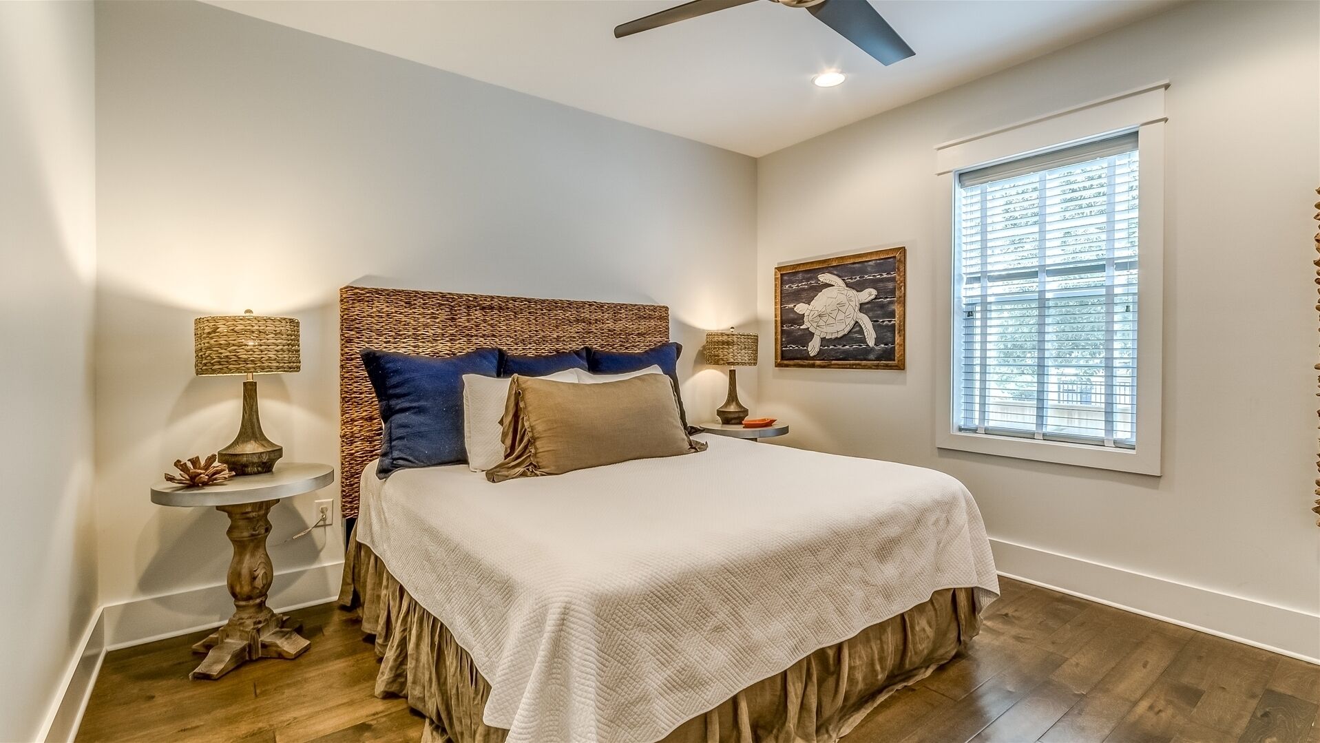 Um quarto com uma cama grande, duas mesas de cabeceira com luminárias, um ventilador de teto, uma janela com persianas e um quadro na parede.