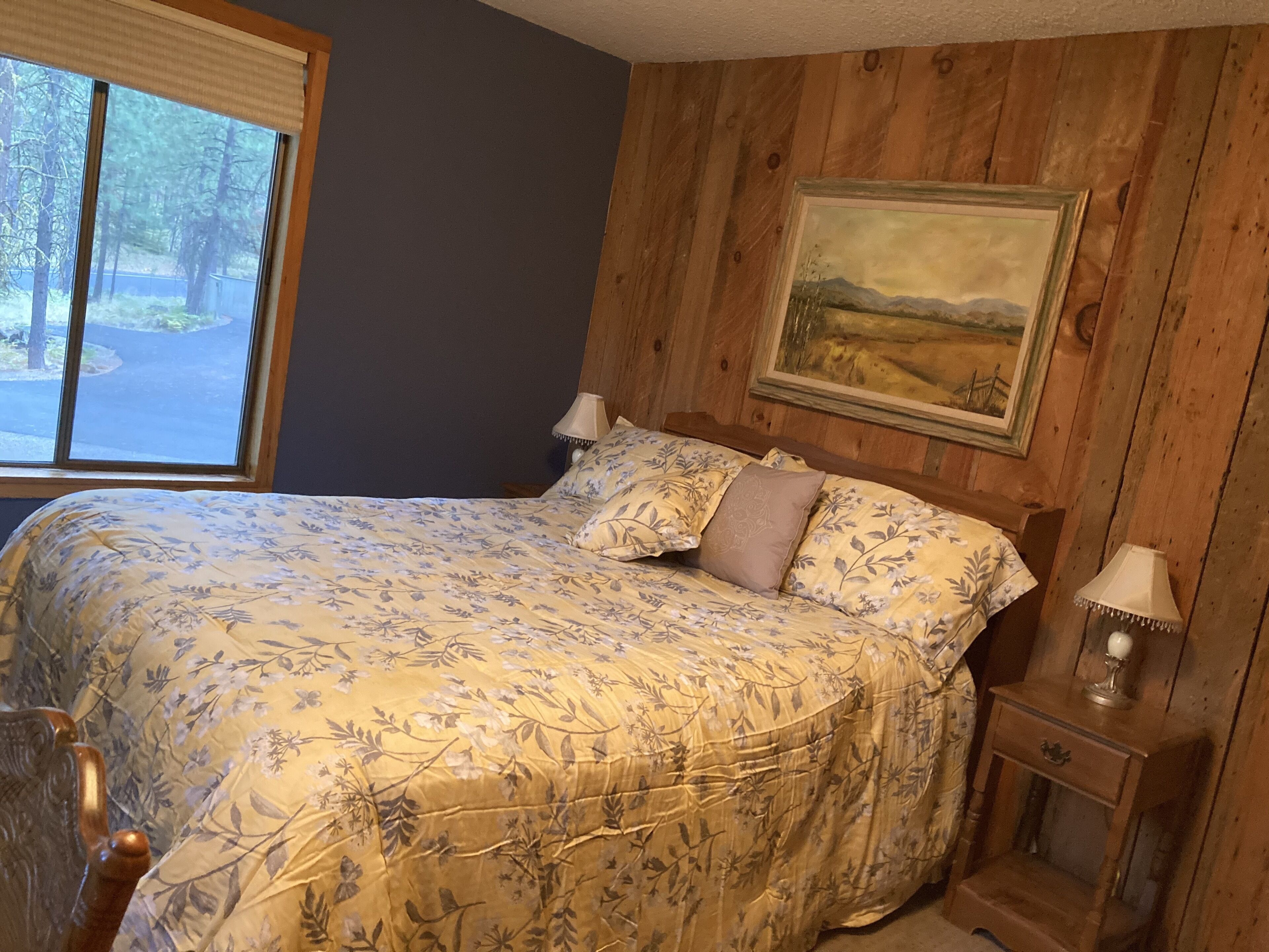 A bedroom with a bed, two bedside tables, a window, and a painting on the wall.