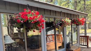 Una terraza cubierta con cestas de flores colgantes, una terraza de madera y una manguera de jardín verde.