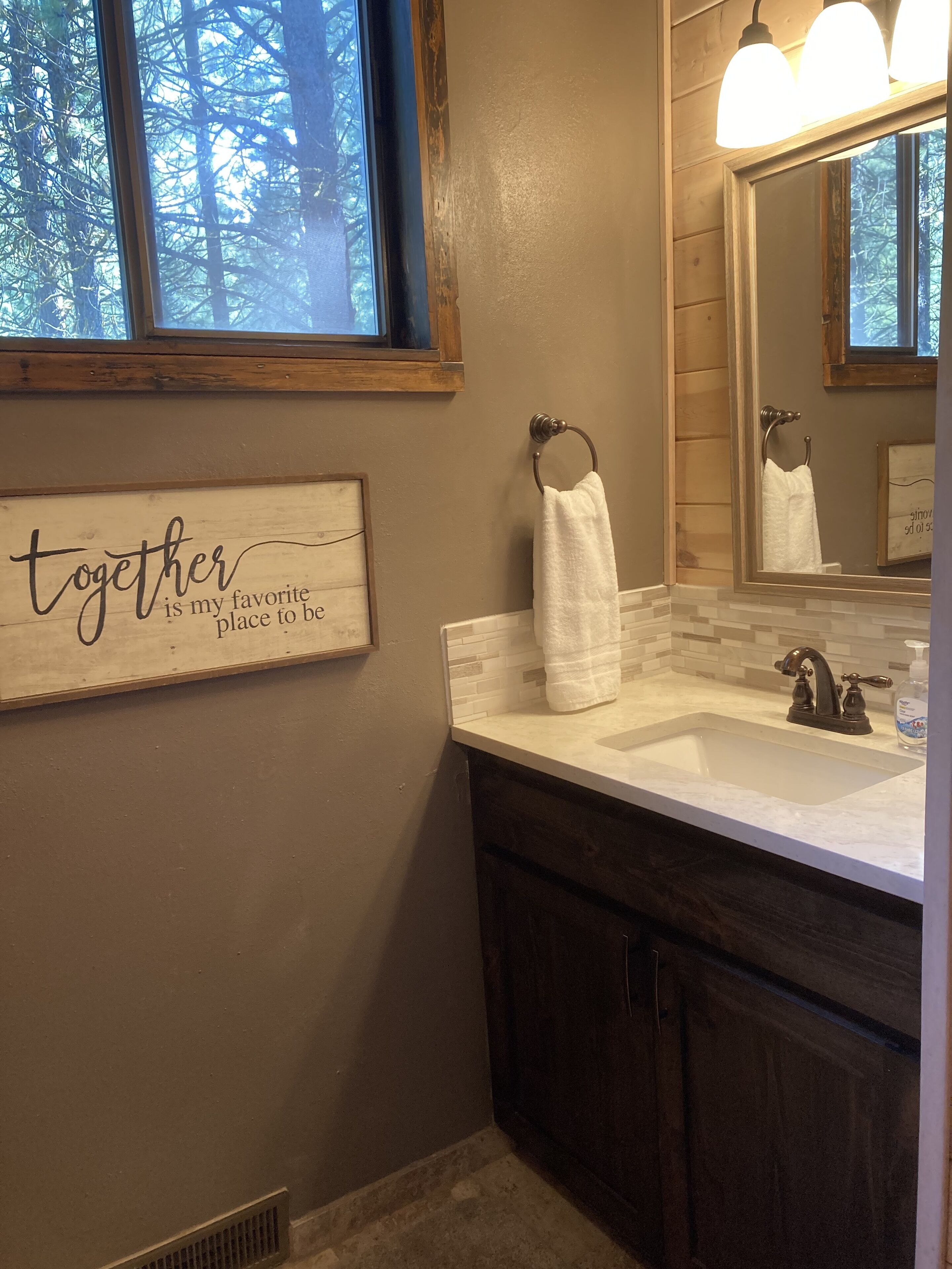 Une salle de bain avec un meuble-lavabo en bois, un évier, un miroir et une fenêtre donnant sur les arbres.