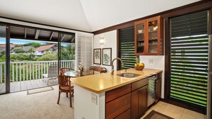 Una cocina con una isla grande, armarios de madera y vista a un balcón con mobiliario exterior.
