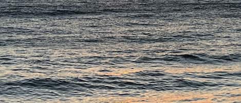 A sunset over the ocean with waves approaching the shore.