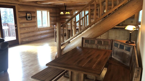 A wooden cabin interior with a staircase, a dining table, and a bench. - King's Deer Lodge in Denali  (Denali)