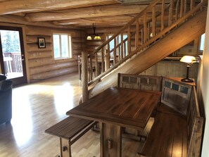 A wooden cabin interior with a staircase, a dining table, and a bench.