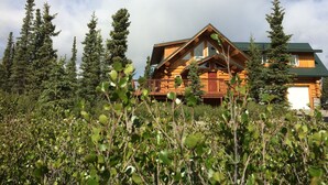 A log cabin with a balcony, surrounded by tall trees and a clear sky. - King's Deer Lodge in Denali  (Denali)