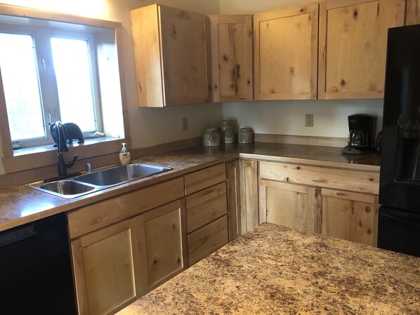 Una cocina con armarios de madera, encimera de granito, refrigerador negro y cafetera.