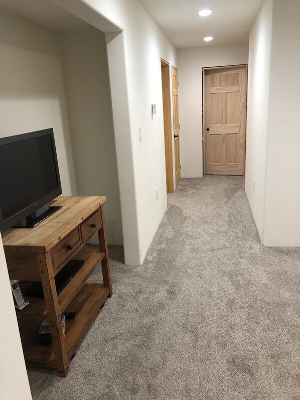 A hallway with a wooden entertainment unit, carpeted floor, and a door at the end.