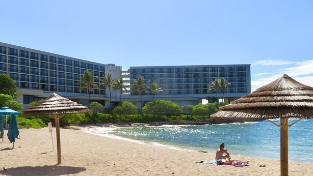 A beach with thatched umbrellas, a sandy shore, and a modern hotel building in the background. -  Closest to Hotel and Beach, Split Air Conditioners (Kahuku)