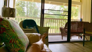 A room with a sofa, a chair, and a view of a balcony with outdoor furniture. -  Closest to Hotel and Beach, Split Air Conditioners (Kahuku)
