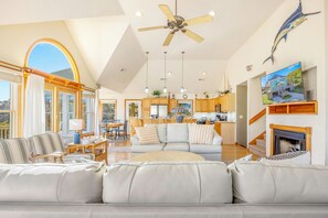 A spacious living room with a large sofa, a dining area with wooden furniture, a kitchen with wooden cabinets, and a ceiling fan. - Oceanview Dog Friendly Home in Waves w/ Private Pool, Hot Tub, and Game Room (Waves)
