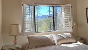 Ein Schlafzimmer mit großem Fenster, einem Bett mit gesteppter Bettdecke, einem Nachttisch mit Lampe und einer Kommode.