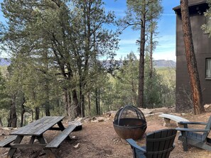 A rustic outdoor seating area with a picnic table and chairs, surrounded by tall trees and a mountain view. - Breathtaking Views of Mogollon Rim  from Large Mountain Home (Payson)