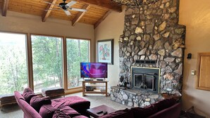 Ein Wohnzimmer mit Kamin aus Stein, einem Fernseher und einem violetten Sofa.