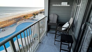 Ein Balkon mit Blick auf Strand und Meer, ein Schwimmbad und zwei Stühle.