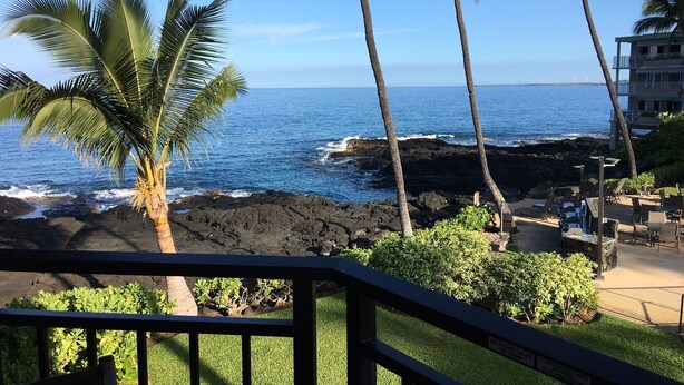 Vista costera con palmeras, olas del océano y un edificio con terraza.