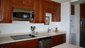 Cocina con armarios de madera, electrodomésticos de acero inoxidable, lavavajillas y encimera con un tarro para cuchillos.
