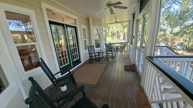 Eine überdachte Veranda mit Holzboden, grün-weißen Geländern und Gartenmöbeln, darunter eine Bank und Stühle.