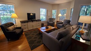 Ein Wohnzimmer mit einer Couch, einem Sessel, einem Couchtisch, einem Fernseher und gemusterten Stühlen.