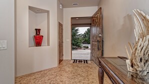 Passadís amb una porta de fusta que dona a l'exterior, un vas vermell a la paret i una taula de fusta amb una peça decorativa.