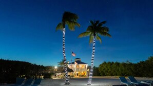 A beachfront hotel with palm trees, a flag, and sun loungers. - Ocean View 2BR - Pool, Private Beach & Near Parks (Tavernier)