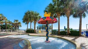 A water fountain with a crown and fleur-de-lis design, surrounded by palm trees and a clear blue sky.
