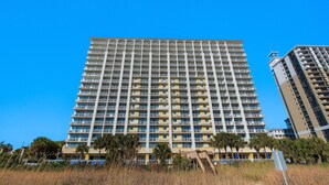 A high-rise building with multiple balconies, a flat facade, and a clear blue sky.