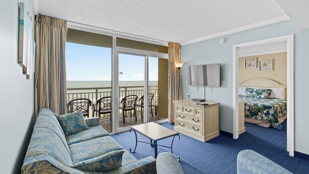 A hotel room with a balcony, a sofa, a TV, a dresser, and a bed with floral bedding.