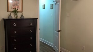 A bedroom with a wooden dresser, a ceiling fan, a framed picture, and a door leading to another room. - Mardi Gras Cottage, 4 km to French Quarter (ARABI)