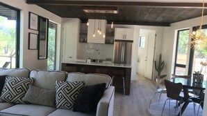Ein modernes Wohnzimmer mit einer Couch, einem Essbereich mit Stühlen, einer Küche mit Kühlschrank und einer Decke mit freiliegenden Balken.