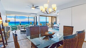 Een ruime woonkamer met een glazen tafel, rieten stoelen en uitzicht op de oceaan.
