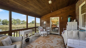 Una terraza de madera con mobiliario de mimbre, una zona de comedor y vistas al exterior.
