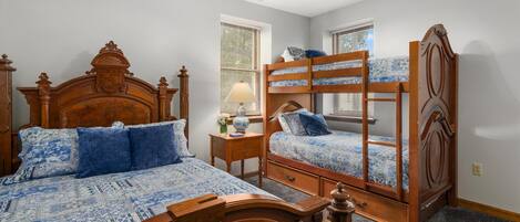 A bedroom with a large bed, a smaller bed, a nightstand, and a window with blinds.