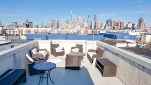 A rooftop terrace with wicker furniture, a round table, and a view of a city skyline. - Spacious 4BD/3Bath, HUGE Rooftop deck and patio. Amazing Views! (Philadelphia)