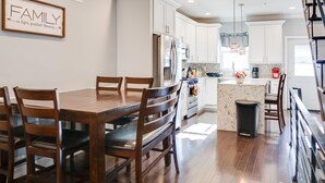 A modern kitchen with white cabinets, stainless steel appliances, and a wooden dining table. - Spacious 4BD/3Bath, HUGE Rooftop deck and patio. Amazing Views! (Philadelphia)