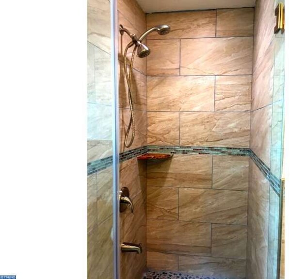 Une douche avec une porte en verre, des murs carrelés et un pommeau de douche.