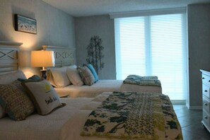 A bedroom with two beds, a nightstand, a lamp, and a window with blinds. - Great Family Retreat w Amazing Views. #11D (Pensacola Beach)