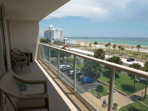 A balcony with wicker chairs, a view of a beach, a parking lot, and a distant pier. - Great Family Retreat w Amazing Views. #11D (Pensacola Beach)