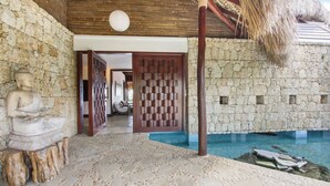 Un espace piscine entouré de murs en pierre, agrémenté d’une statue de Bouddha, doté d’un plafond en bois et surmonté d’un toit de chaume.
