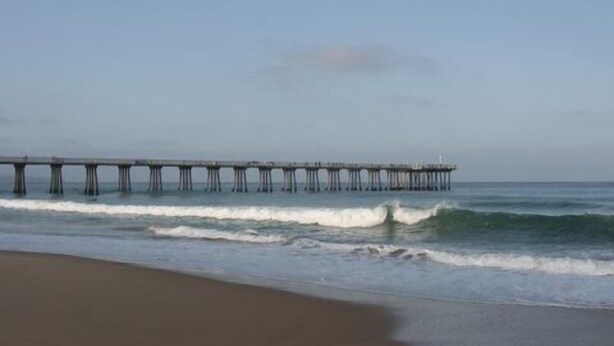 Un muelle se adentra en el océano, con olas rompiendo sobre la orilla.