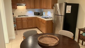 Una cocina con armarios de madera, un refrigerador de acero inoxidable, un microondas y una mesa de comedor con sillas.