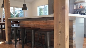 A modern kitchen with wooden accents, a bar area with stools, and a large window providing natural light.
