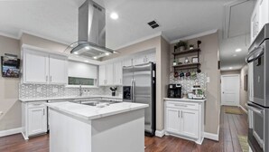 Et moderne køkken med hvide skabe, en central ø, rustfrie stålemmer og et mønstret backsplash.